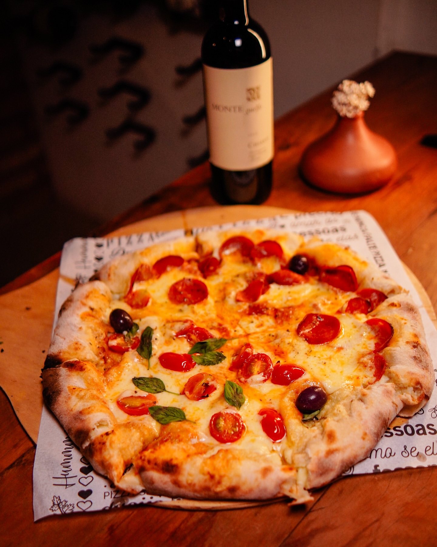Pizza meio margherita, meio calabresa, com uma garrafa de vinho