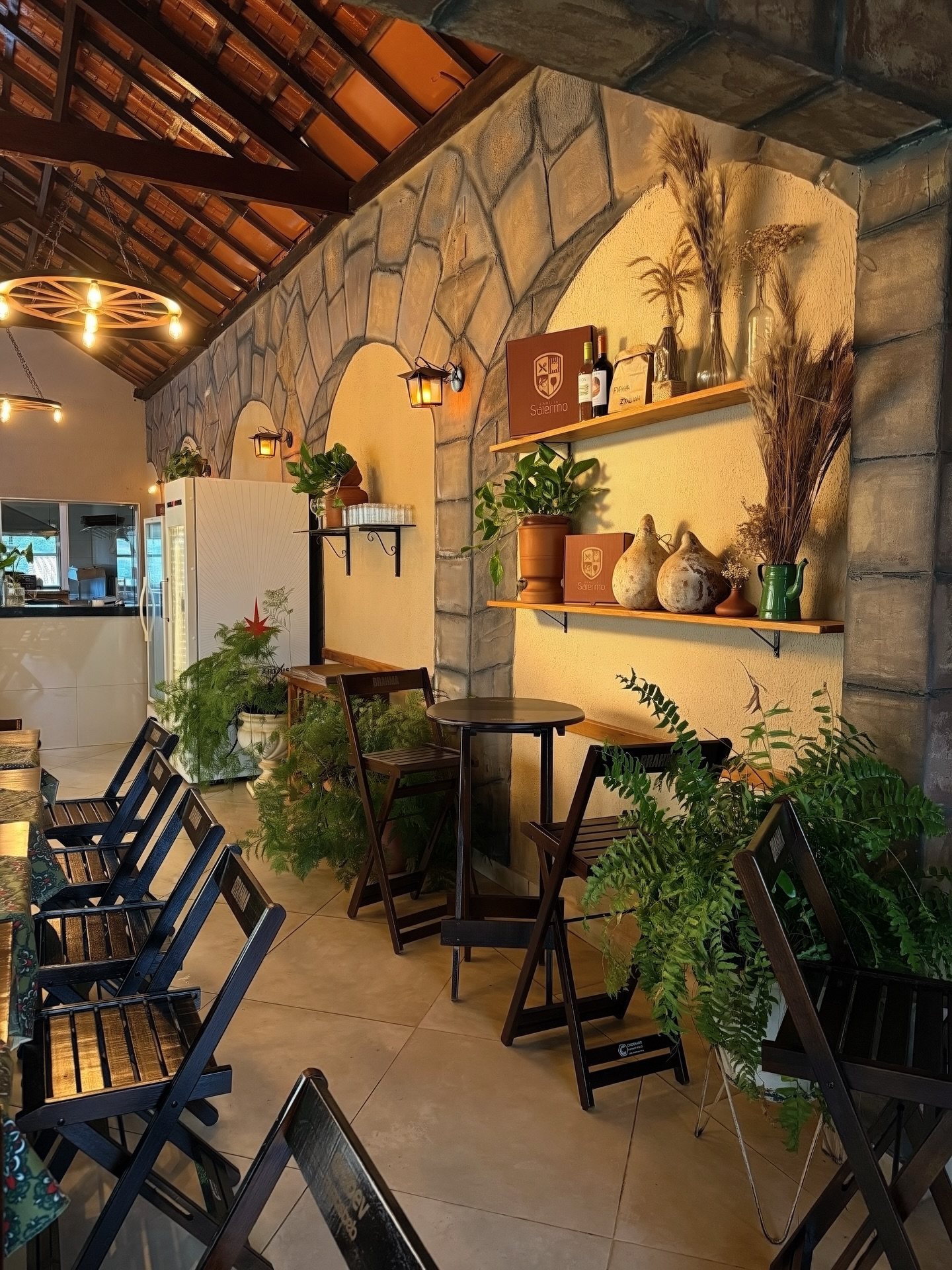 Salão da pizzaria com arcos de pedra, prateleiras com vinhos e luminárias acesas